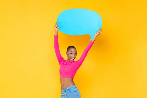Photo of Beautiful excited African American woman smiling and raising empty speech bubble isolated on colorful studio yellow background