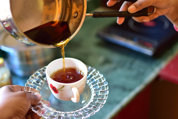 istock Young woman using kettle for make tea or black coffee on kitchen at room interior background.Women's hands pour water from a teapot into a cup. Blurred, flares effect 1317894305
