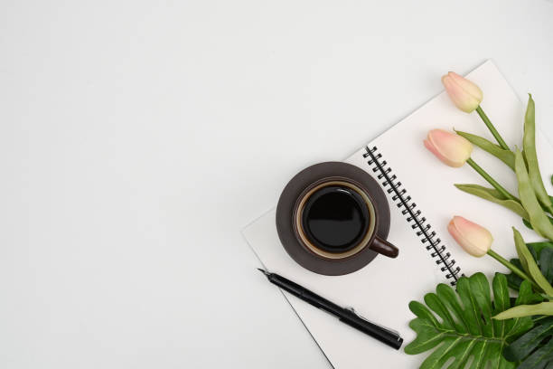 istock Above view coffee cup, notebook, pen, pink tulip and copy space on white desk. 1317898407