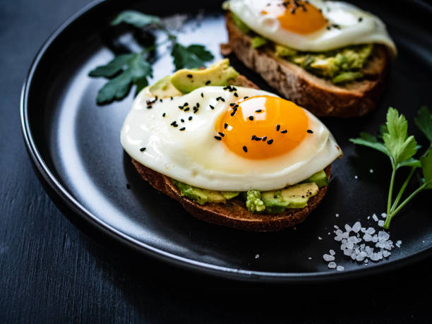istock Continental breakfast - sunny side up eggs on toasted bread with avocado on black background 1317899223