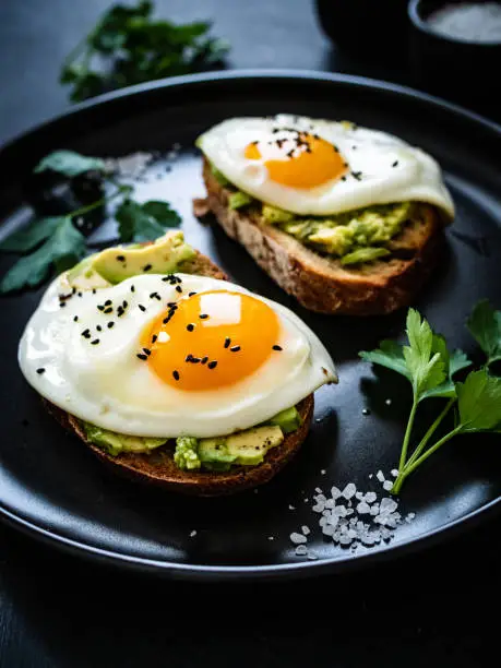 Continental breakfast - sunny side up eggs on toasted bread with avocado on black background