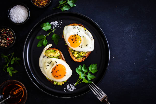 istock Continental breakfast - sunny side up eggs on toasted bread with avocado on black background 1317899269