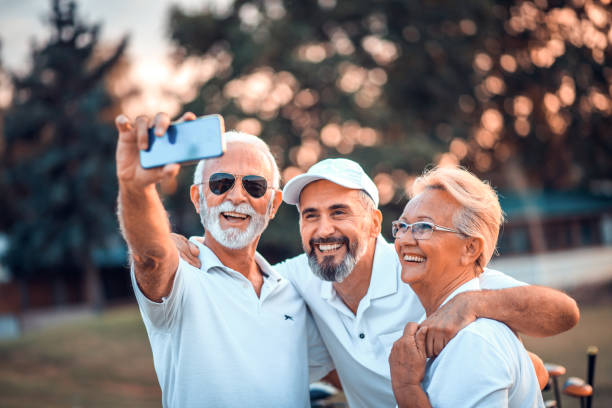 старшие игроки в гольф, используя телефон и принимая автопортрет. время воспоминаний. время воспоминаний. - старшие мужчины стоковые фото и изображения