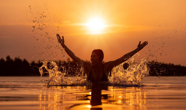 silhouette of woman splashing water in infinity pool at sunset