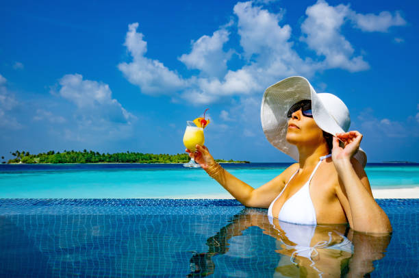 элегантная женщина, наслаждающаяся солнцем и пьют пина колада в курортном бассейне на острове мальдивы - poolside enjoyment sensuality blue стоковые фото и изображения