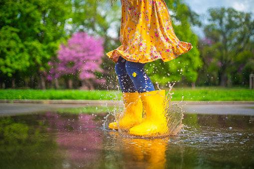 Happy child girl with yellow rubber boots  jumping in puddle at the spring day walk.