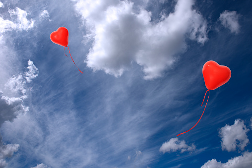 Two red heart-shaped balloons floating in a blue sky with copy space.