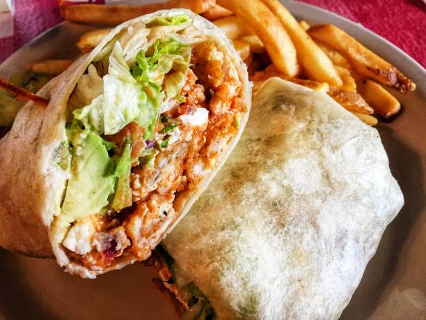 Buffalo Chicken Blue Cheese Wrap Spicy buffalo sauce coated crispy fried chicken breast, topped with blue cheese, avocado and lettuce. Fold it all up in an oversized tortilla and cut in half. Some fusion cuisine for you. wrap sandwich photos stock pictures, royalty-free photos & images