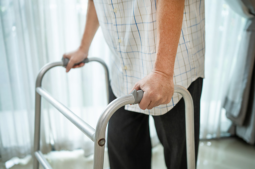 Close up hand of Asian Senior elderly disabled man patient walk slowly with walker at nursing home. Older handicapped male have weak leg use Zimmer frame to support. Medical therapy insurance concept.