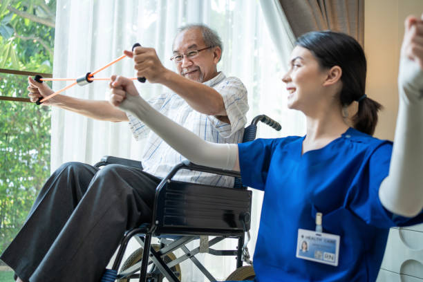 Asian Disabled senior elderly man on wheelchair doing physiotherapist with support from therapist nurse. Older handicapped man using resistance stretch band exercise for patient in home nursing care
