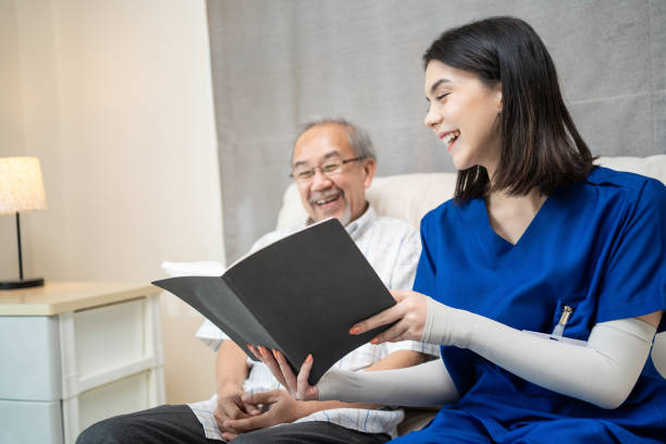 enfermeira asiática no asilo cuidando de idosos idosos sentados no sofá. médico terapeuta cuidador lendo um livro para pacientes com deficiência mais velho. conceito de serviço de seguro médico. - listening child grandfather family - fotografias e filmes do acervo