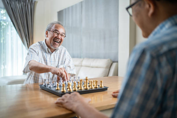 asian senior starszy mężczyzna spędza wolny czas, zostaje w domu po przejściu na emeryturę. szczęśliwy uśmiechnięty starzec cieszyć się działalnością w domu gry w szachy z przyjacielem razem. szpitalna opieka zdrowotna i koncepcja medyczna - play time zdjęcia i obrazy z banku zdjęć