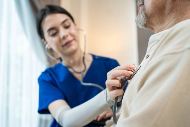 enfermera asiática en el asilo de ancianos discapacitados en silla de ruedas. el médico terapeuta mide la frecuencia cardíaca por estetoscopio en pacientes mayores. concepto de servicio de seguro médico - escuchando el latido del corazón fotografías e imágenes de stock