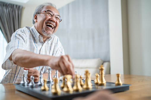 Portrait of Asian Senior Elderly male spend leisure time, stay home after retirement. Happy smiling Old man enjoy activity in house play chess game with friend. Hospital Healthcare and medical concept