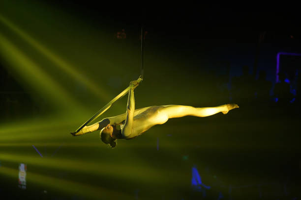 acrobate féminin font la fente russe sur le cerceau aérien dans le costume d’étape d’or rétroéclairé dans la lumière jaune - 16711 photos et images de collection