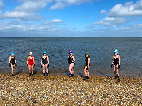 A group of mature female friends standing on the beach before swimming in the sea