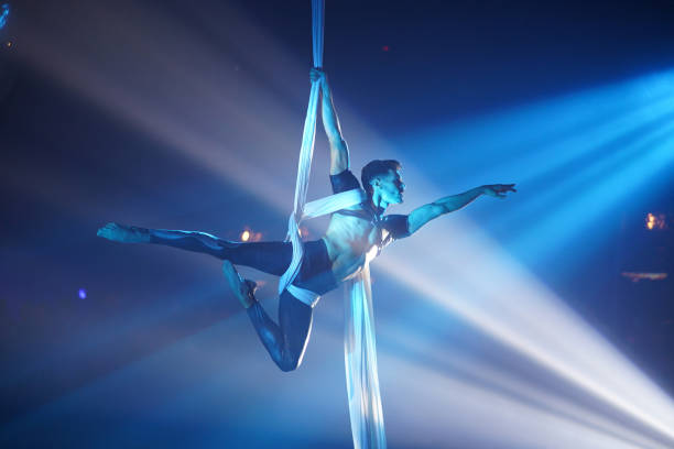 Athletic gymnastic Brazilian man doing aerial silks performance backlit with white and blue light Sport training gym and lifestyle concept. gymnastics stock pictures, royalty-free photos & images