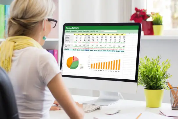 Photo of Woman working with data and graphs in spreadsheet document on desktop computer