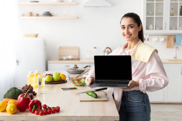 istock Woman showing laptop with empty screen for mockup in kitchen 1317932100