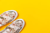Pair of female's new stylish slip-ons with floral ornament on a yellow background. Flat lay. Copy space. Close up of shoes toes