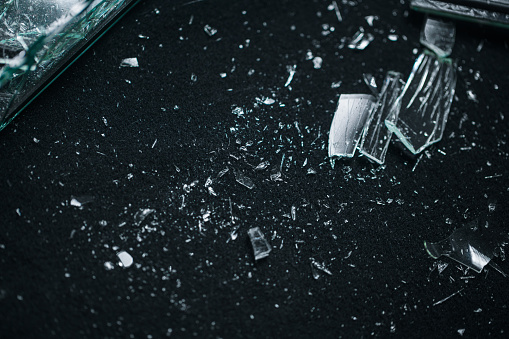 Small pieces of broken glass lie on a black background. The glass fell to the black floor and shattered into small pieces. The photo was taken in a photo studio with a professional light.