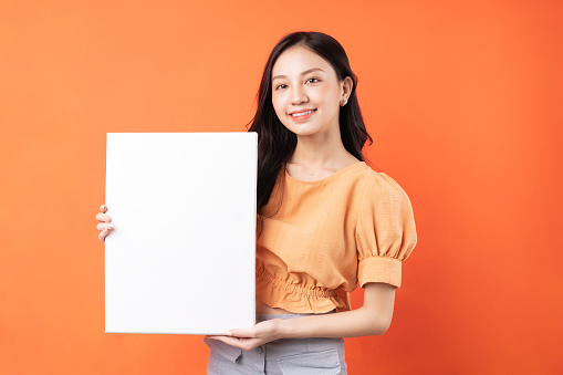 Young Asian woman holding white board on orange background