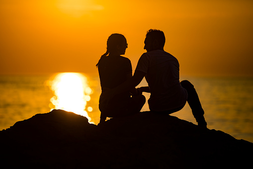 Silhouette of a Young Couple Sitting on Coastline During Sunset.