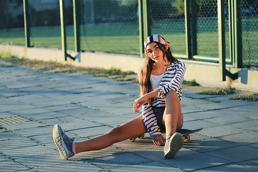 Teenage girl sitting on a skateboard in front of a stadium