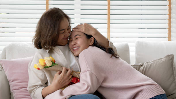 attractive beautiful asian middle age mum sit with grown up daughter give gift box and flower in family moment celebrate mother day. overjoy bonding cheerful kid embrace relationship with retired mom. - latin american and hispanic ethnicity senior adult mature adult couple imagens e fotografias de stock