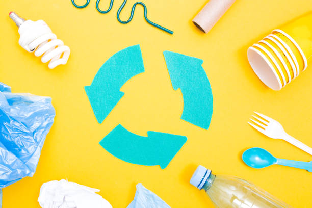 istock various trash and a recycling sign in the middle, yellow background, copy space, top view, bottles, disposable tableware, cardboard and paper, eco friendly, plastic bag 1317948913