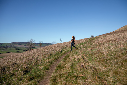 Wide shot of a female runner confidently running on a footpath on Roseberry Topping, Middlesborough, North Yorkshire.