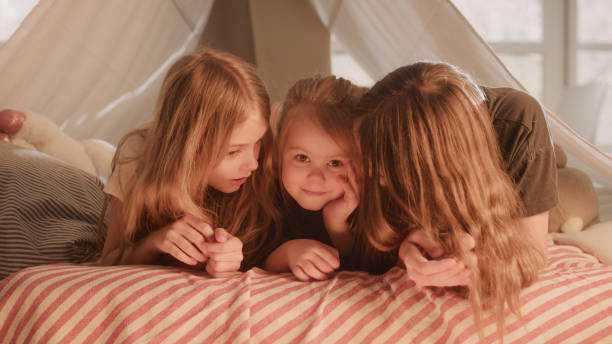 istock Three sistrers lying on cozy, canopy bed. Looking at camera and smiling 1317951782