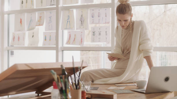 istock Female fashion designer at work. Creating new collection, picking projects hanging on a window 1317952897