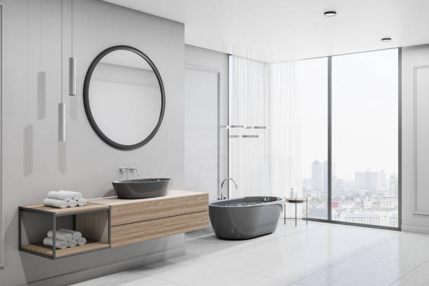 istock Modern spacious bathroom with city view from bug window, glossy floor, black bath and round mirror over black sink 1317955780