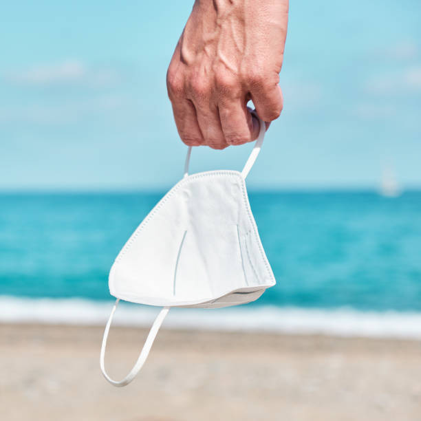 istock man with a FFP2 face mask in his hand on the beach 1317961447