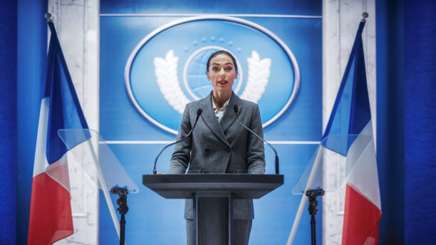 istock Organization Female Representative Speaking at Press Conference in Government Building. Press Office Representative Delivering a Speech at Summit. Minister at Congress. Backdrop with French Flags. 1317961713