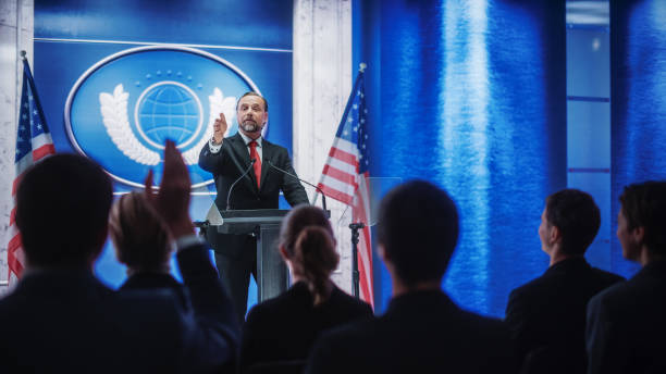 istock Inspiring Organization Representative Speaking at a Press Conference in Government Building. Press Officer Delivering a Speech at a Summit. Minister at Congress. Backdrop with American Flags. 1317961760