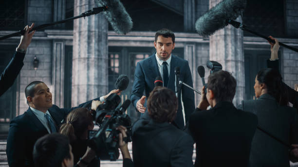 istock Young Organization Representative Answering Press Questions and Giving Interview Outside a Parliament, Court or Other Government Building. Press Officer or Businessman Crowded by News Journalists. 1317961773