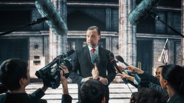 istock Organization Representative Answering Press Questions and Giving Interview Outside a Parliament, Court or Other Government Building. Press Officer or Businessman Crowded by News Journalists. 1317961780