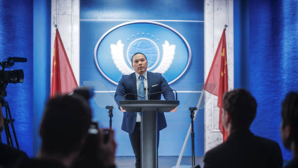 istock Chinese Organization Representative Speaking at Press Conference. Press Officer Delivering a Speech at Summit. Minister Speaking at Congress Hearing. Backdrop with People's Republic of China Flags. 1317961828