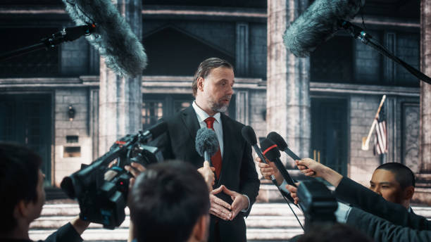 istock Organization Representative Answering Press Questions and Giving Interview Outside a Parliament, Court or Other Government Building. Press Officer or Businessman Crowded by News Journalists. 1317961849