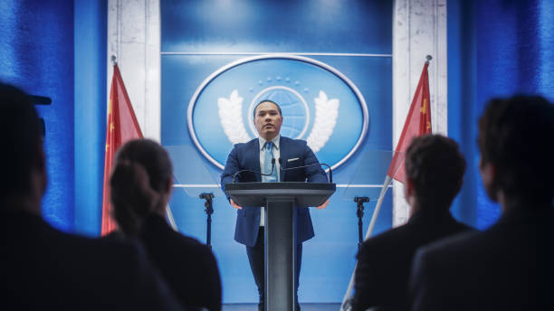 istock Chinese Organization Representative Speaking at Press Conference. Press Officer Delivering a Speech at Summit. Minister Speaking at Congress Hearing. Backdrop with People's Republic of China Flags. 1317961896