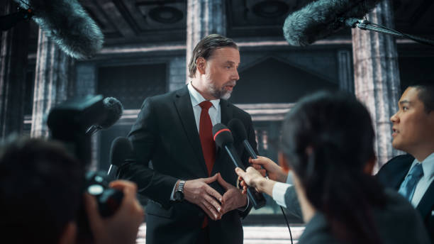 istock Organization Representative Answering Press Questions and Giving Interview Outside a Parliament, Court or Other Government Building. Press Officer or Businessman Crowded by News Journalists. 1317961914