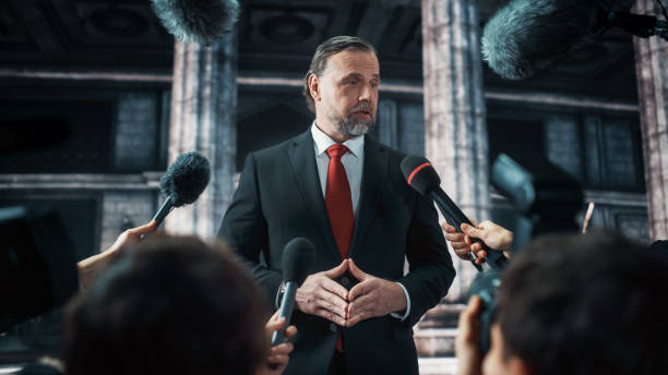 istock Organization Representative Answering Press Questions and Giving Interview Outside a Parliament, Court or Other Government Building. Press Officer or Businessman Crowded by News Journalists. 1317961929