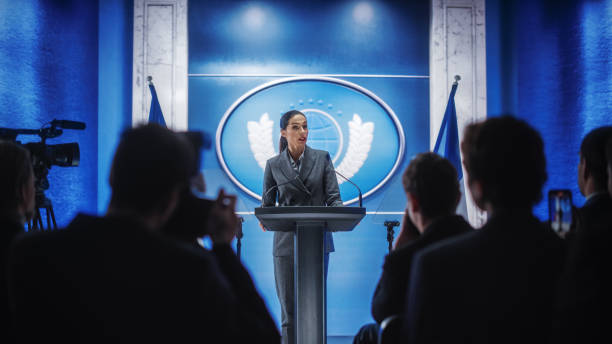 istock Organization Female Representative Speaking at Press Conference in Government Building. Press Office Representative Delivering a Speech at Summit. Minister at Congress. Backdrop with French Flags. 1317961936