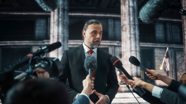 istock Organization Representative Answering Press Questions and Giving Interview Outside a Parliament, Court or Other Government Building. Press Officer or Businessman Crowded by News Journalists. 1317961939