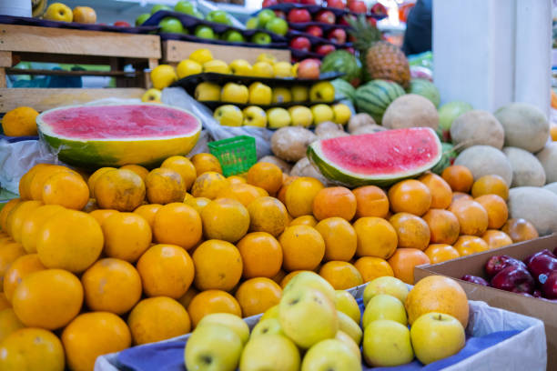 Colorful fruit stand with fresh oranges, sliced watermelons, yellow apples, melons, and more. Juicy-looking fruit for sale on stall inside classic Mexican market. Healthy food