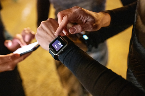 Close-up of young people standing together using their smart devices after a workout session. Group of women checking their fitness progress on smartwatch and mobile phone after training session.
