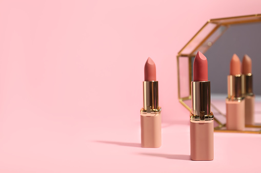 Different lipsticks near mirror on pink background, space for text