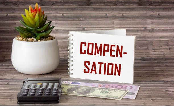 istock The word COMPENSATION is written on a notepad. Euro and dollar banknotes, calculator and cactus lie on a wooden table 1317963712